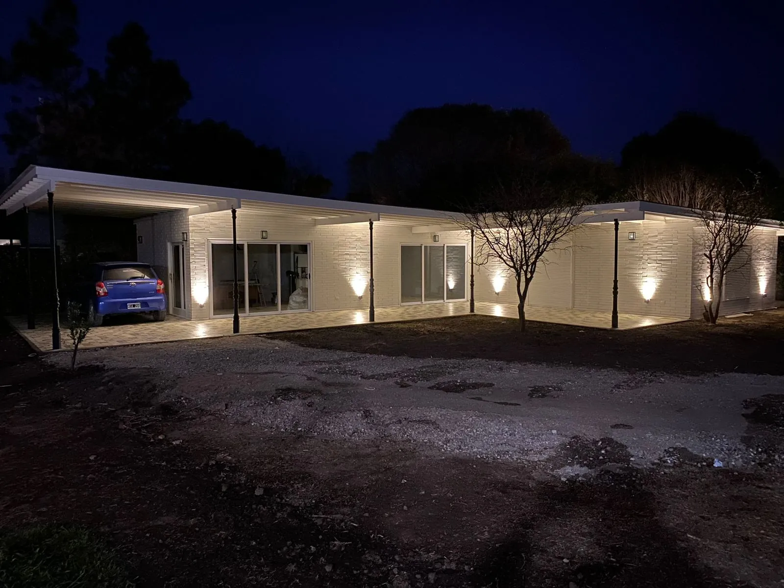White wooden block home at night with warm uplighting